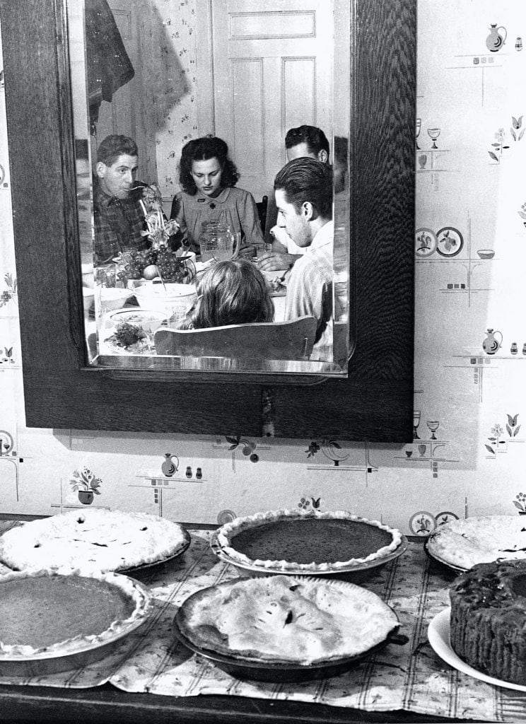 vintage photo of family eating with 6 pies on table behind them.