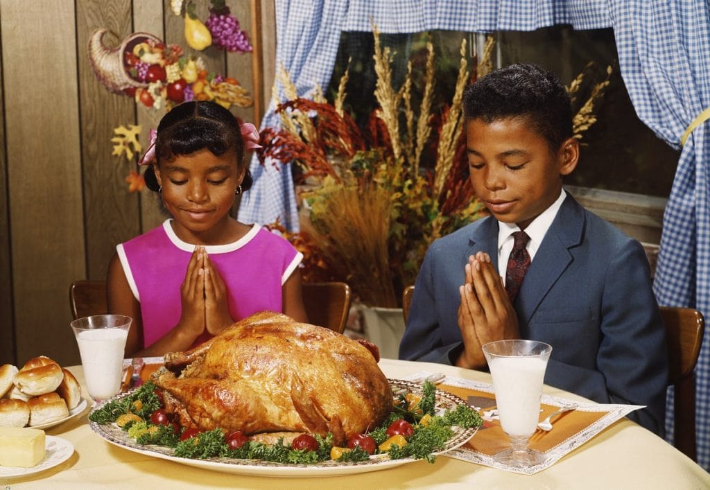 vintage photo of 2 children praying with turkey in front of them.