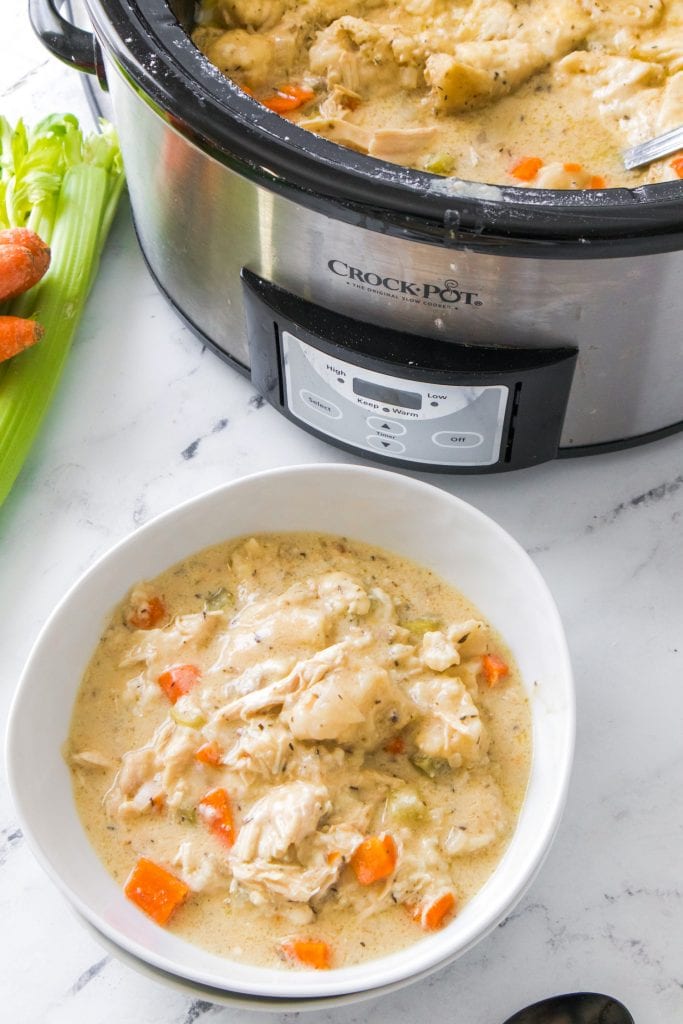 white bowl filled with chicken and dumplings next to crock-pot on table.