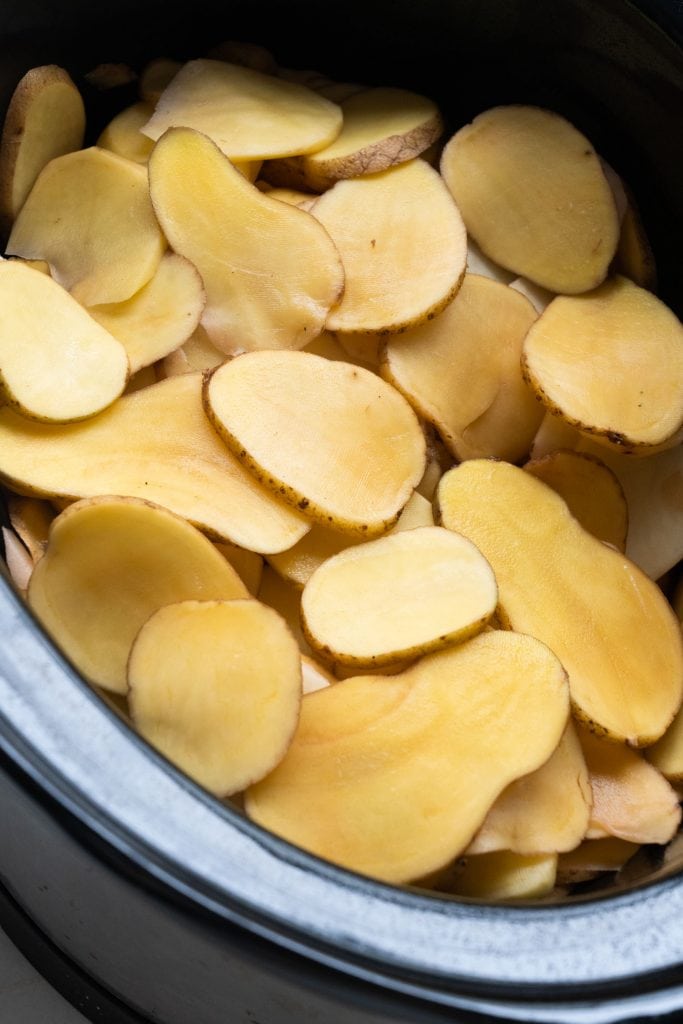 slices of potatoes in bottom of slow cooker.