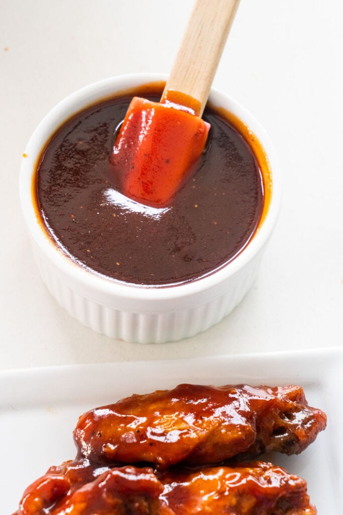 small bowl of bbq sauce next to chicken wings.