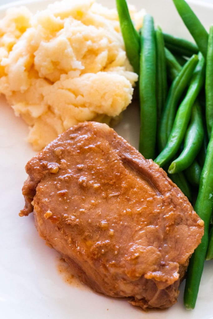 pork chop and gravy on plate next to green beans.