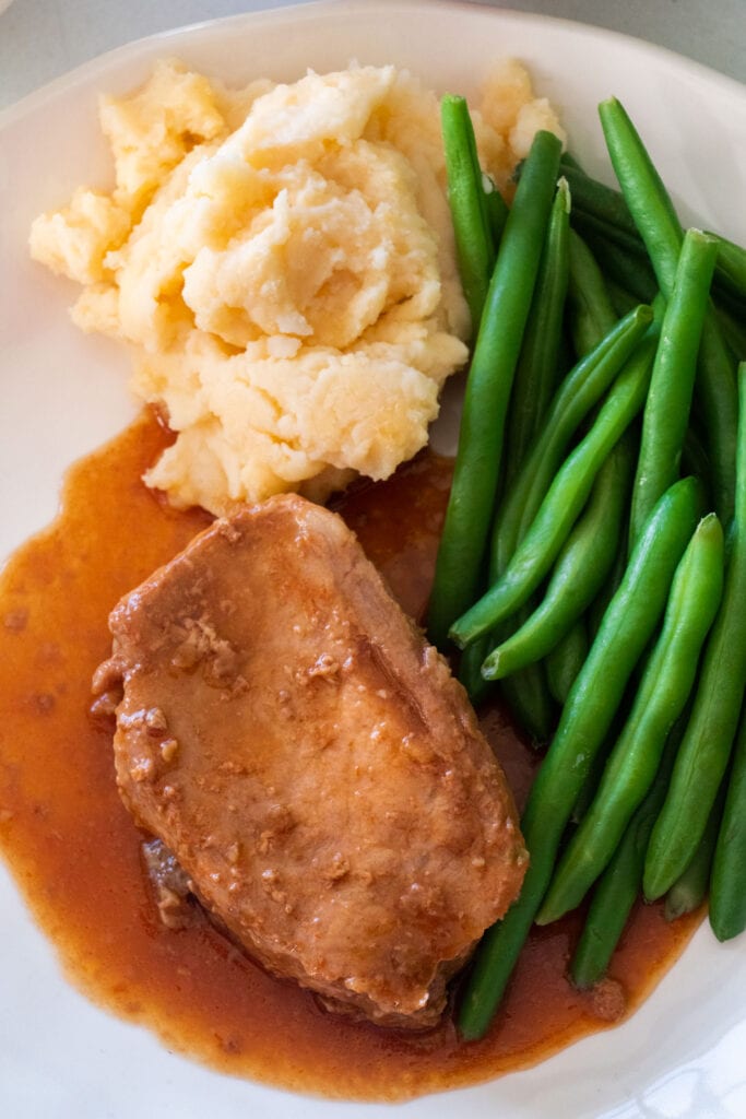 slow cooker pork chops on plate next to mashed potatoes and green beans.