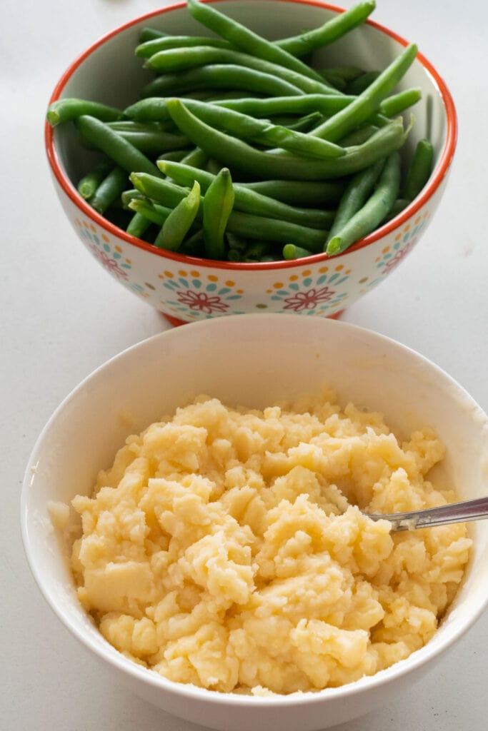 bowls of mashed potatoes and green beans on tale.