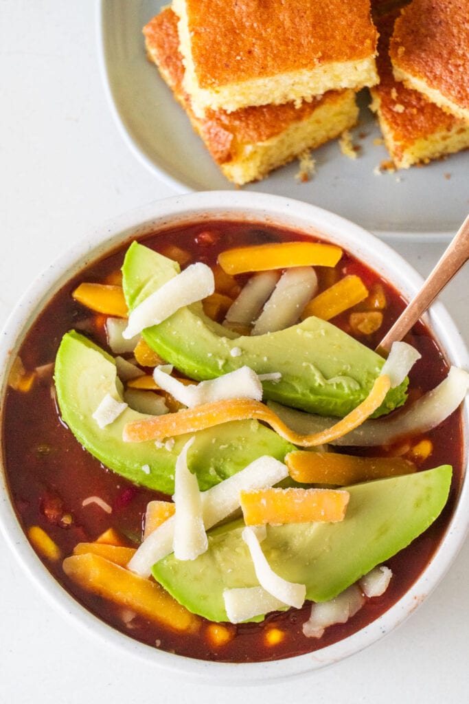 bowl filled with chili with slices of avocado and shredded cheese on top.