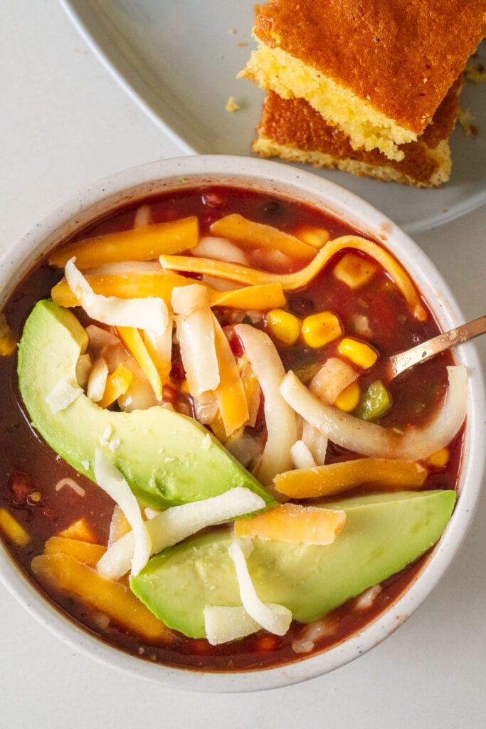 bowl of chili in bowl with cheese and avocado on top.