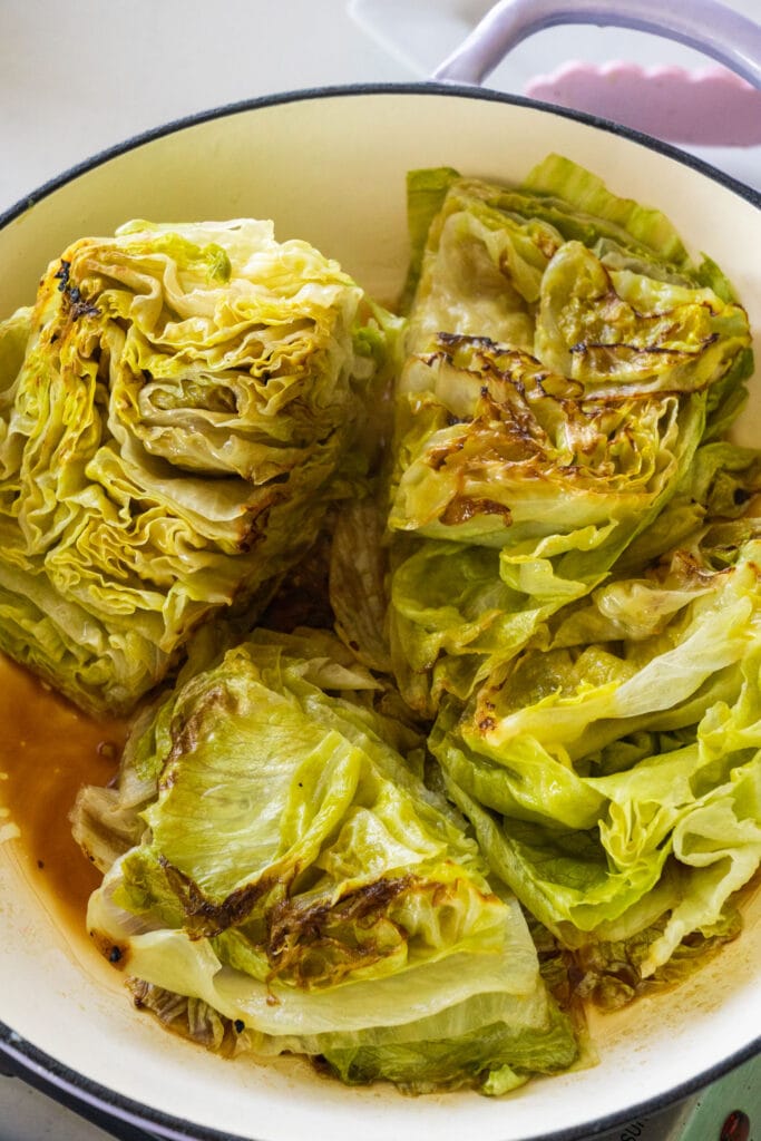 cooked lettuce in brown broth in pan.