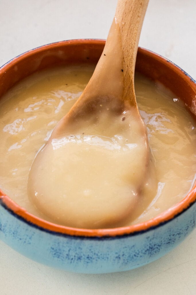homemade gravy in a bowl with wooden spoon in it.