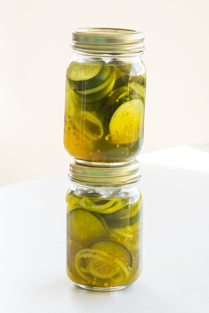 2 mason jars of pickles on top of each other on table.