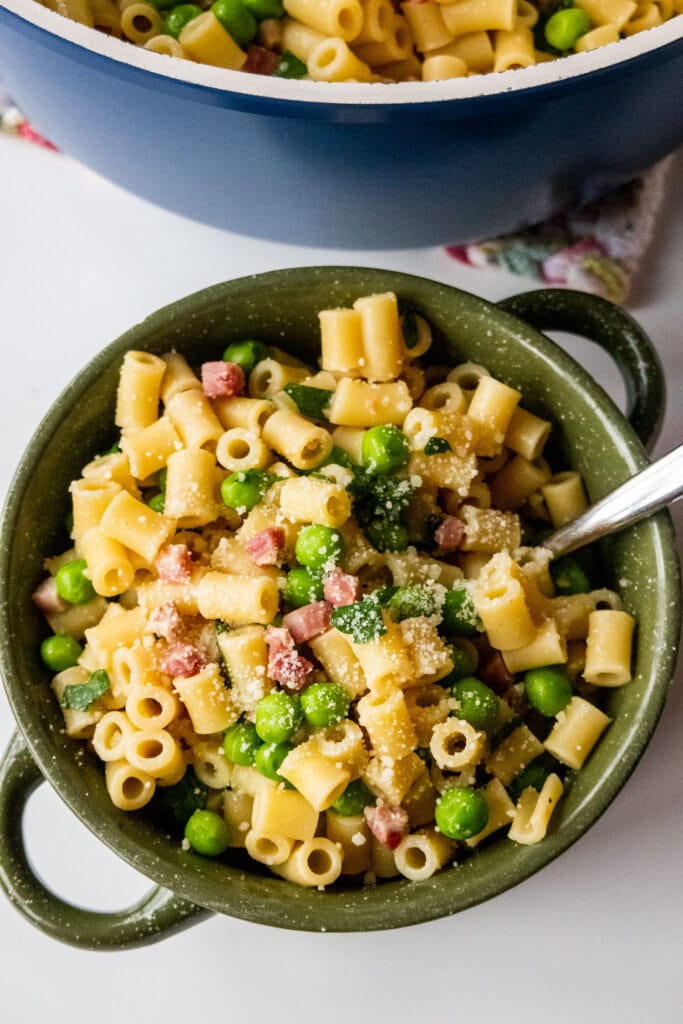 bowl filled with pasta and peas with grated cheese on top.