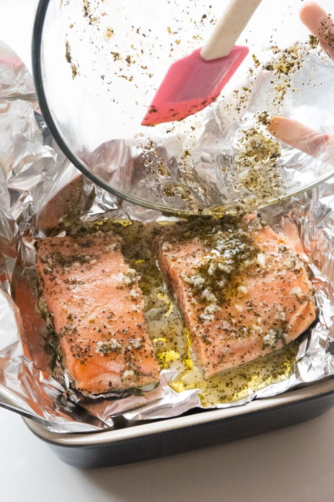 olive oil marinade being poured onto salmon in baking dish.