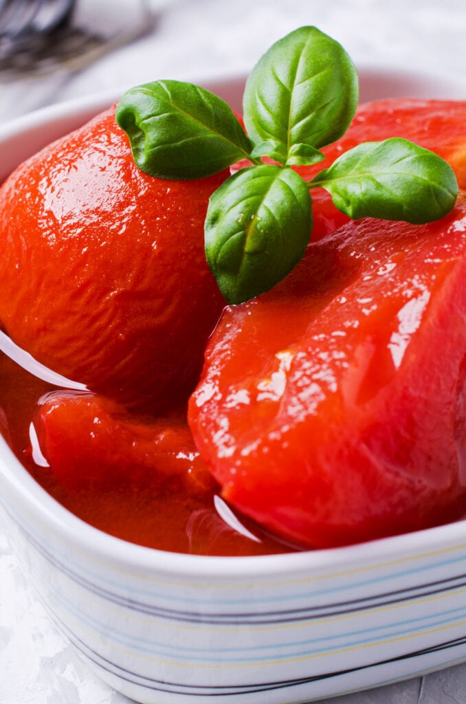 whole peeled tomatoes in bowl with fresh basil on top.