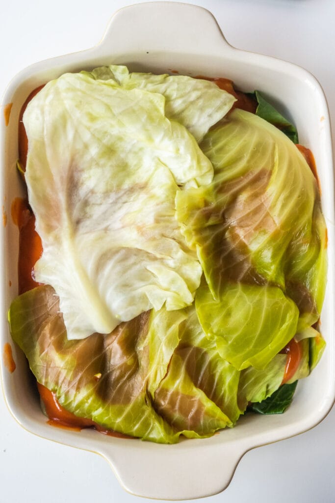 cabbage leaves placed on top of rolls in baking dish.