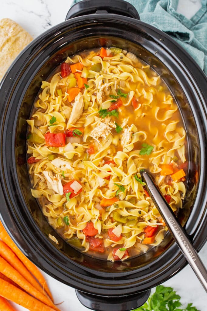 italian noodle soup in slow cooker with spoon going in.
