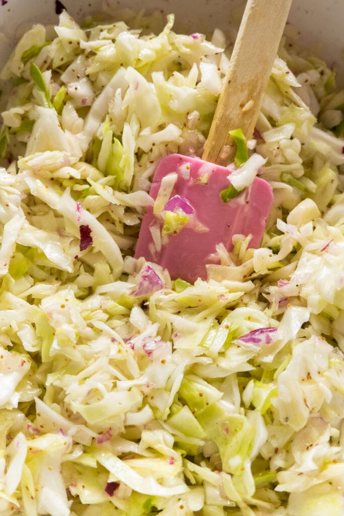 pink spatula mixing coleslaw in bowl.