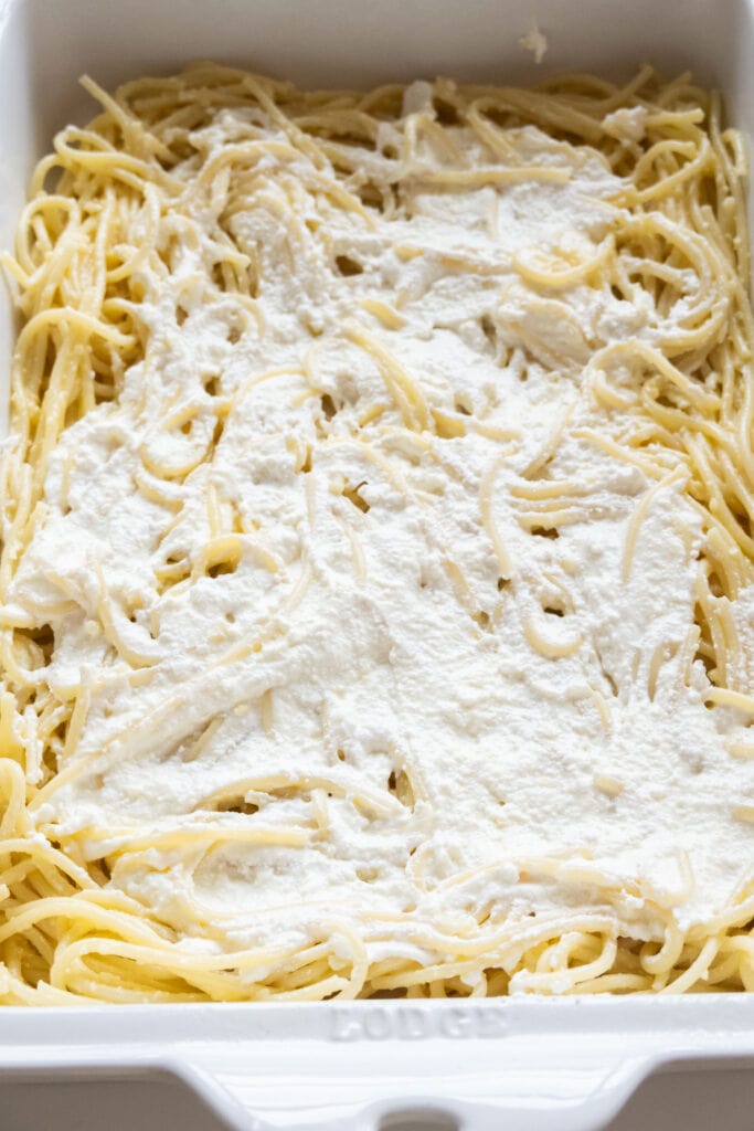 ricotta cheese added on spaghetti in baking dish.