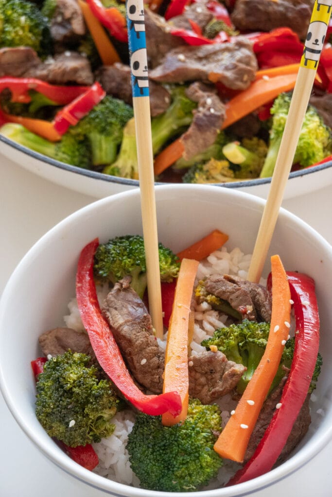 bowl of beef and broccoli on top of rice with chopsticks.