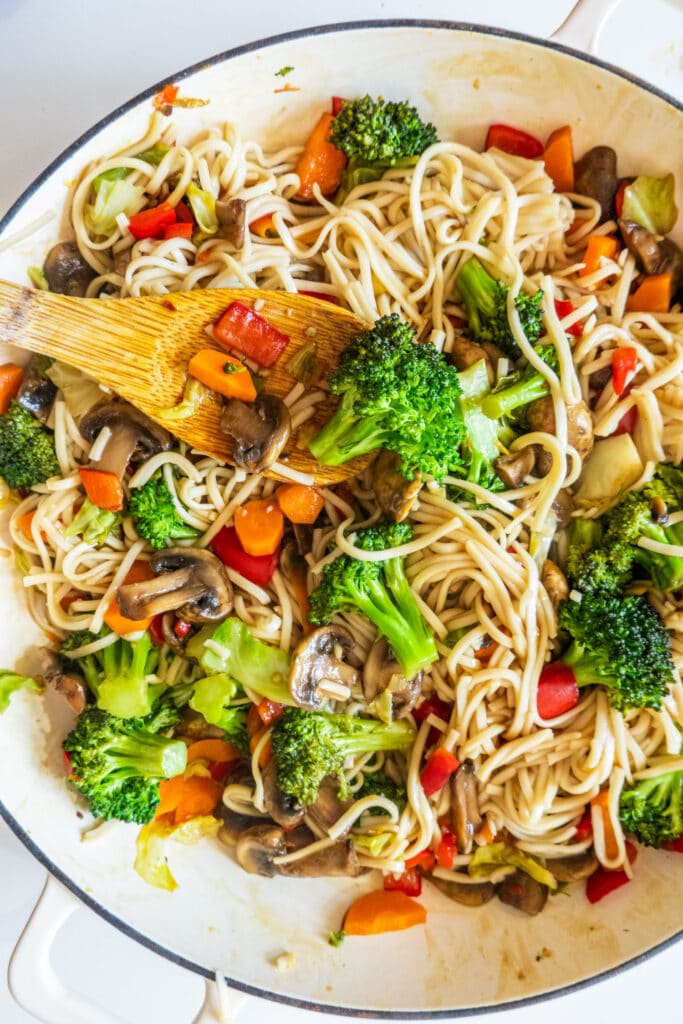 spoon stirring lo mein noodles and vegetables in skillet.