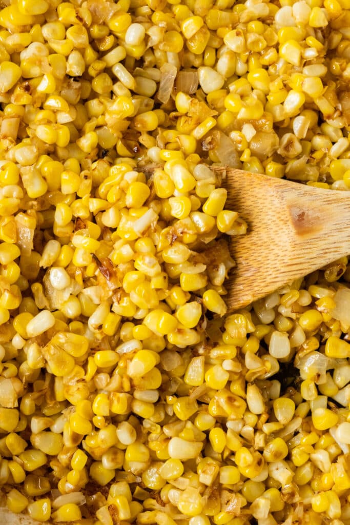 skillet filled with fried corn and onions with spoon in it.