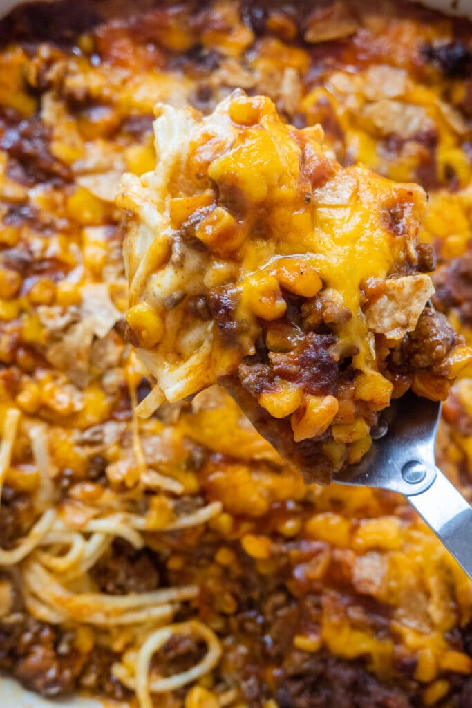 spoon lifting up cheesy taco spaghetti casserole out of baking dish.