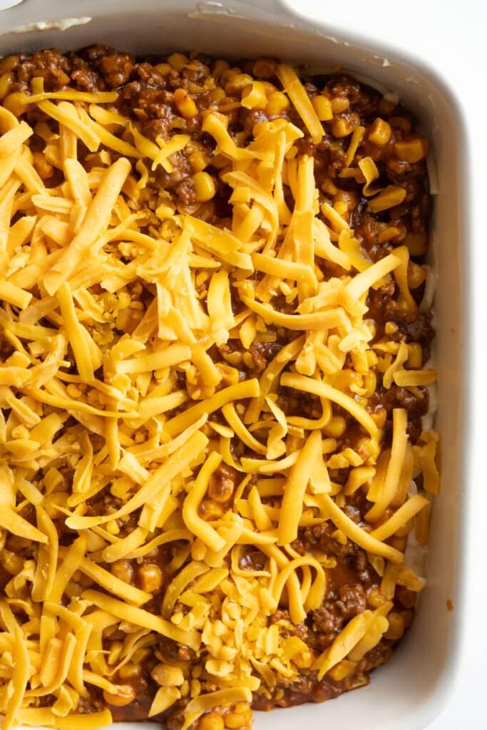 shredded cheese on top of casserole, uncooked, in baking dish.