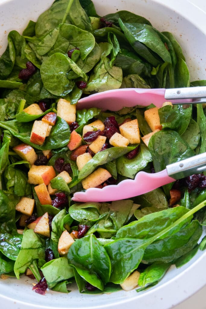 spinach salad in bowl with tongs.