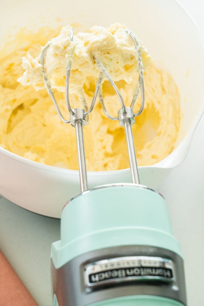 hand mixer creaming together sugar and butter in white bowl. 