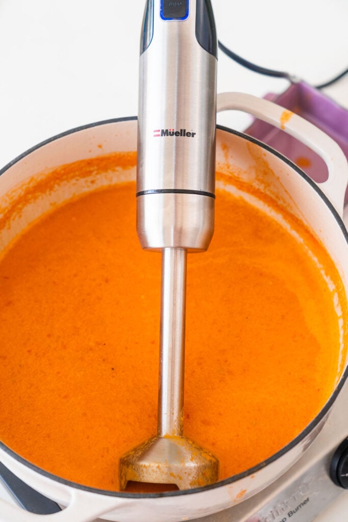 immersion blender in pot with creamy smooth soup.