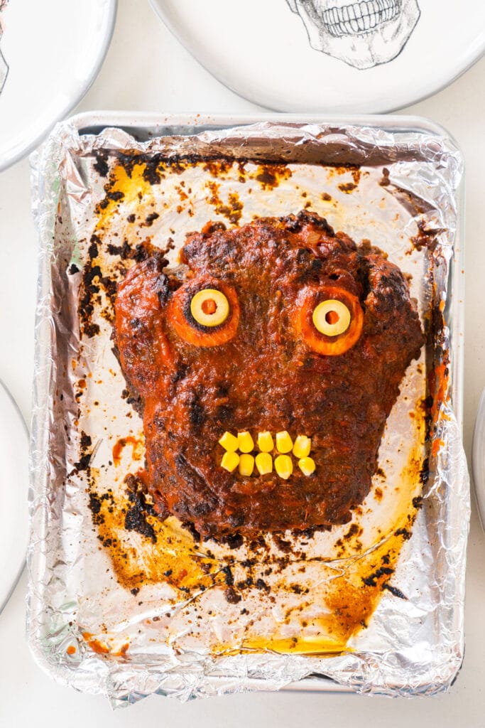 zombie head meatloaf next to plates on table, ready to serve.