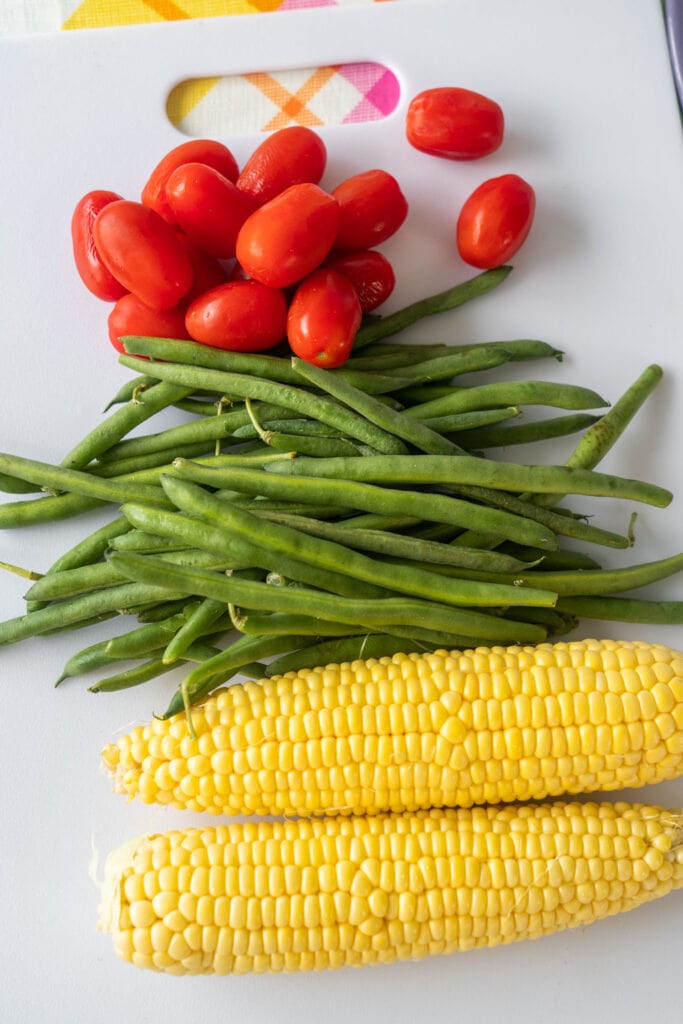 green beans, tomatoes and corn on white cutting board.