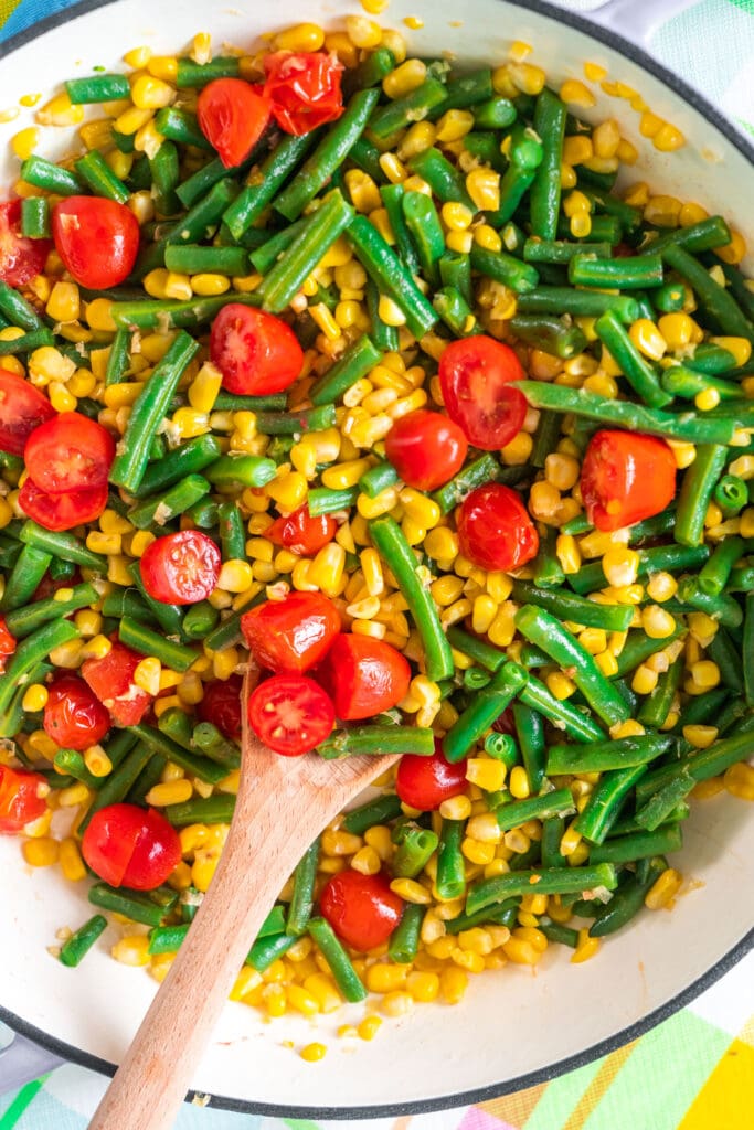 fresh green beans, corn and tomatoes with spoon inside skillet.