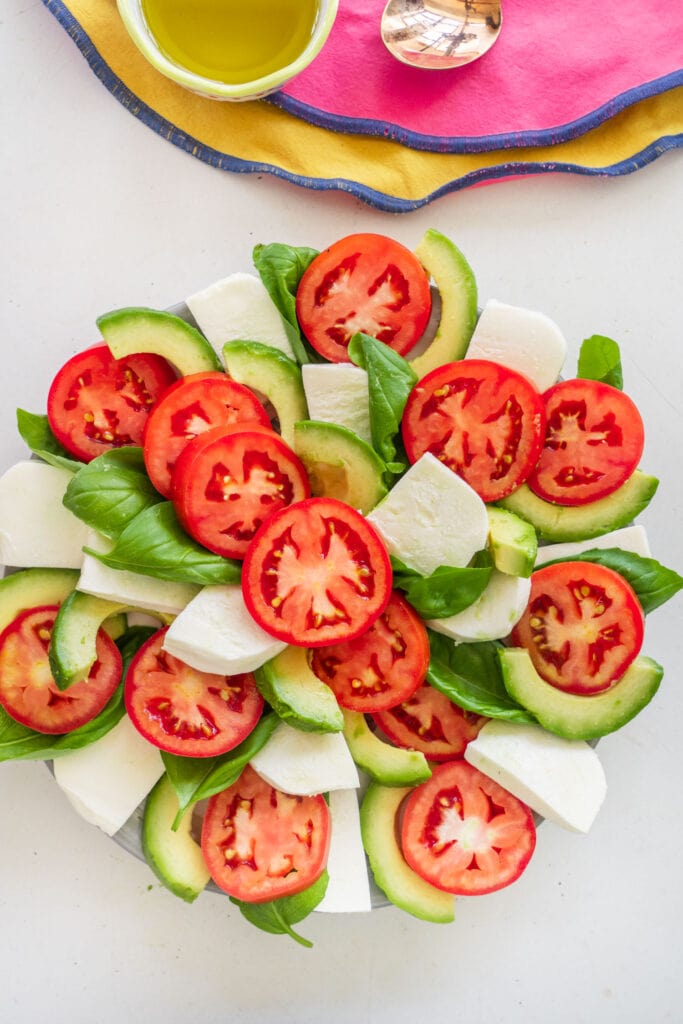 tomatoes, avocado, mozzarella cheese and basil in spiral shape on plate to make a salad.
