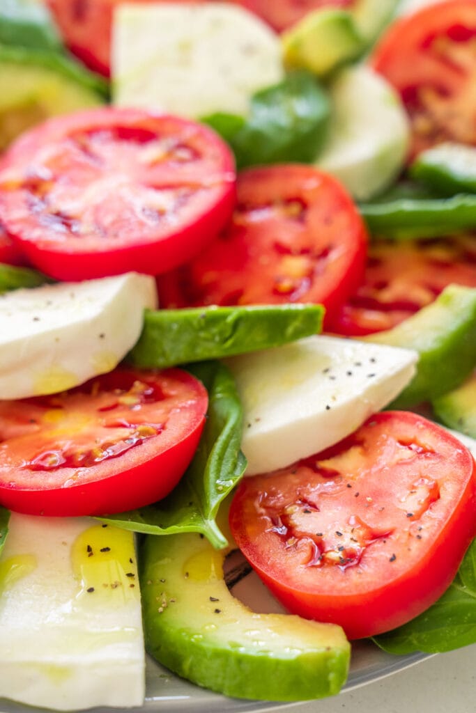 closeup of tomato mozzarella salad with avocado with olive oil on it.