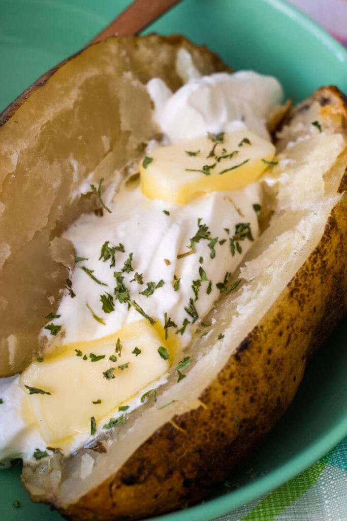 closeup of baked potato with butter and sour cream on top.