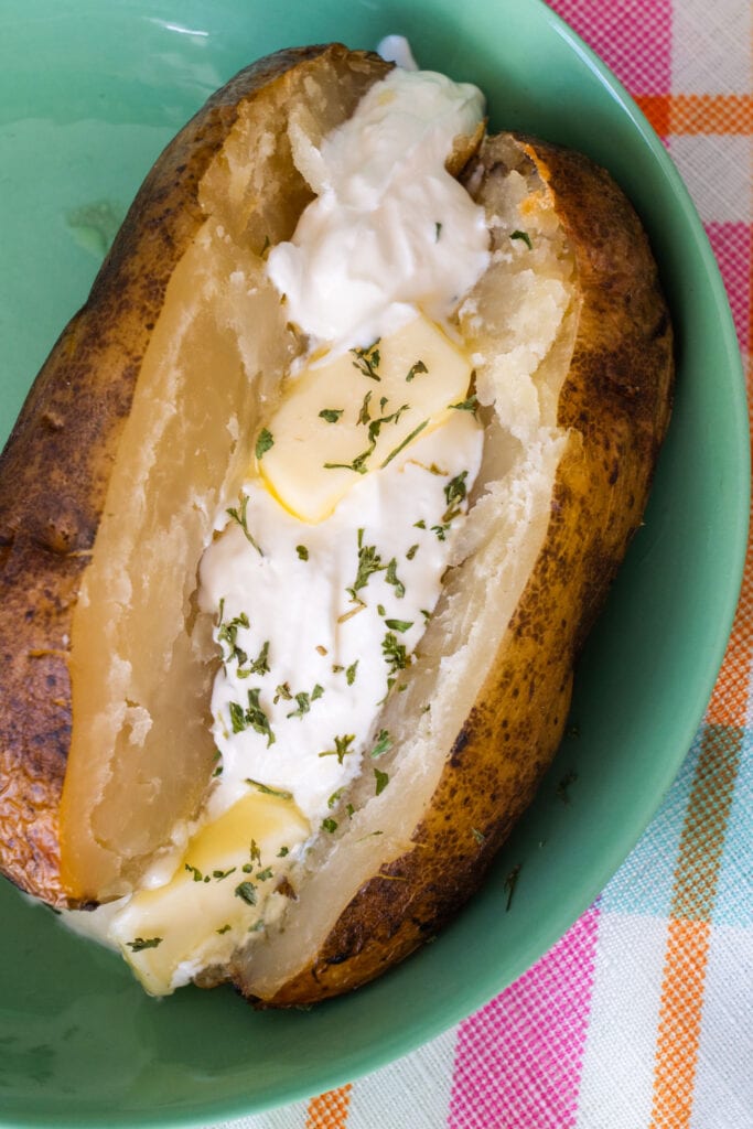 baked potato on green plate with sour cream and butter on it.