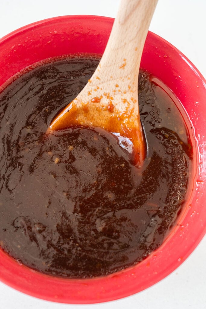 spoon stirring bbq sauce in red bowl.