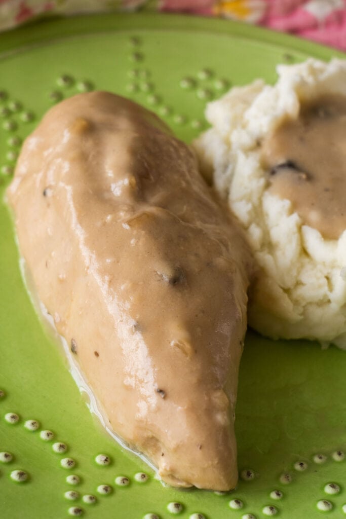closeup of chicken breast next to mashed potatoes with gravy on it.