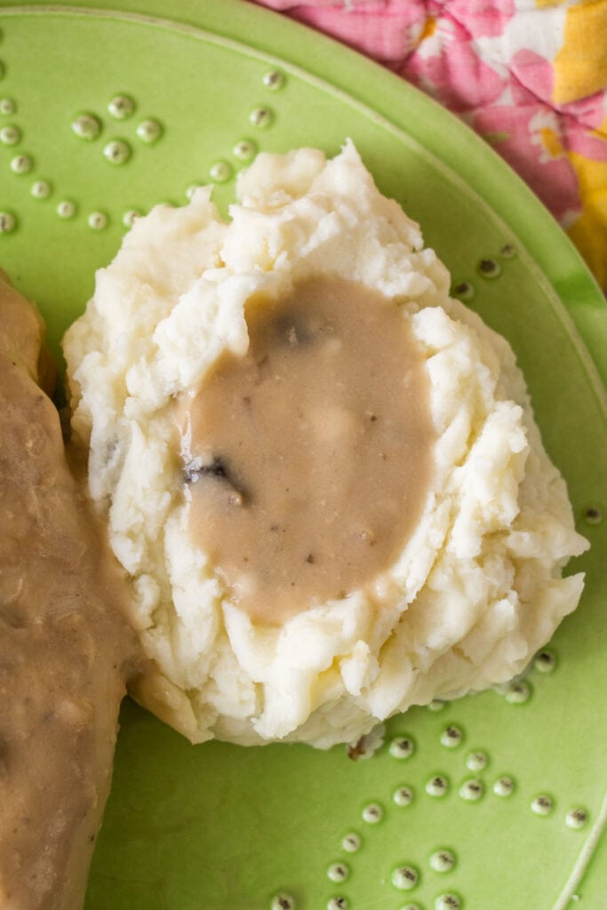 mashed potatoes next to chicken on plate with gravy.