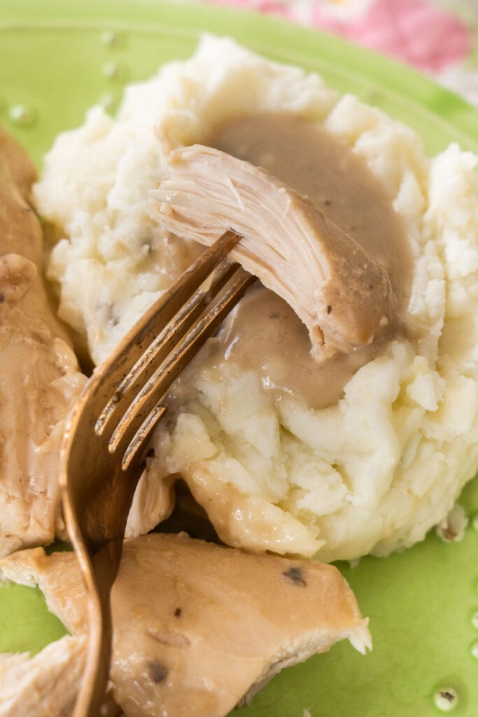chicken on fork on top of mashed potatoes and gravy.