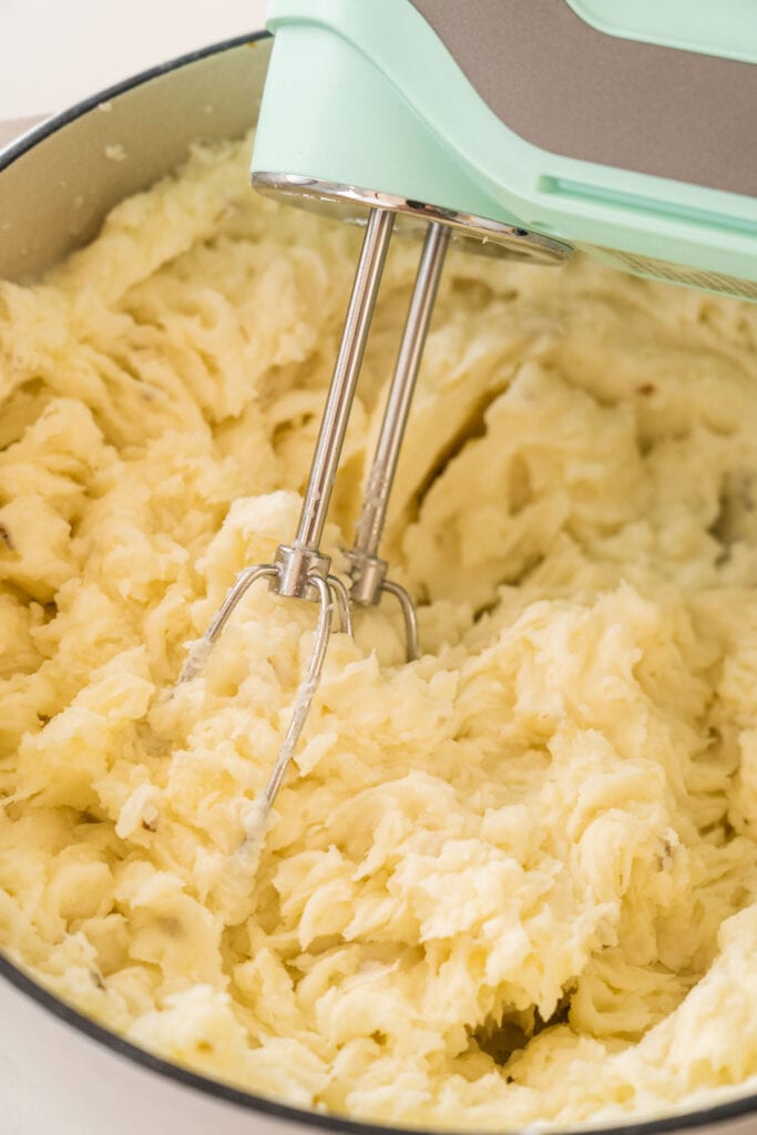 electric mixer mixing mashed potatoes in pot.