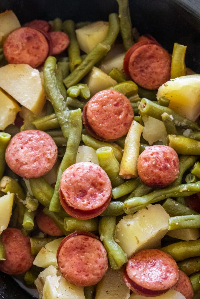 pieces of kielbasa sausage on green beans and potatoes in slow cooker.