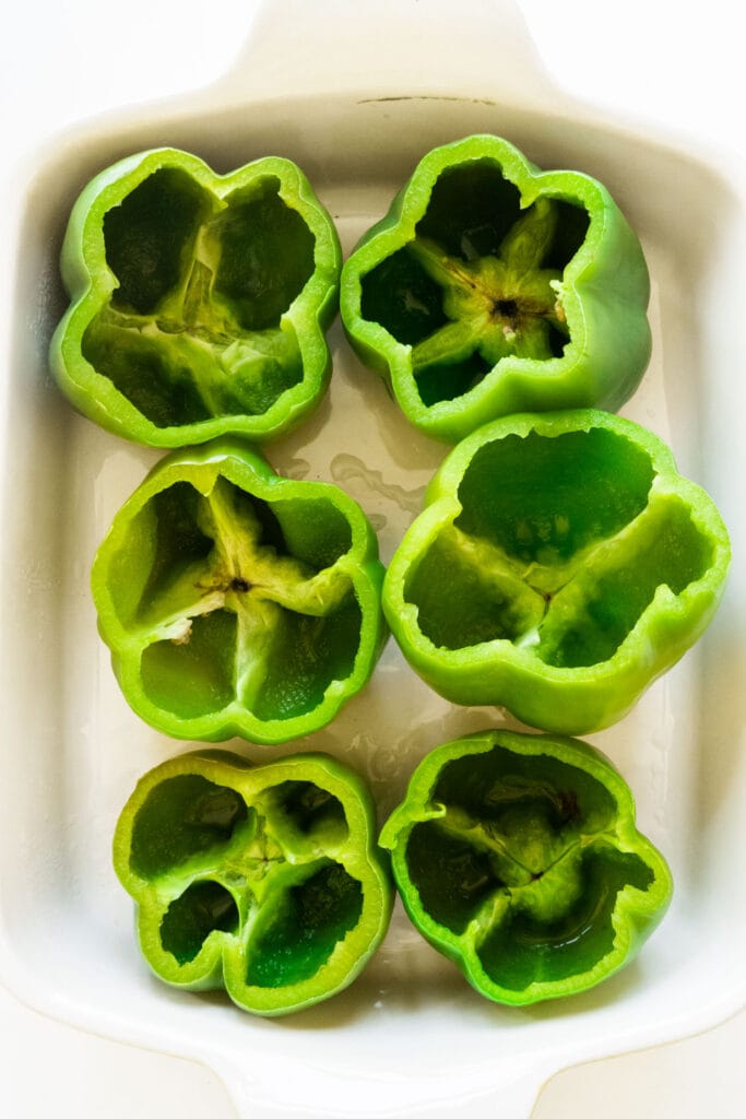 peppers with tops cut off in baking dish.
