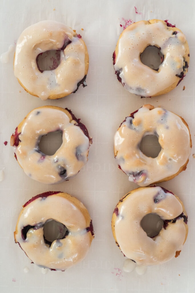 blueberry donuts with icing on top of wax paper.