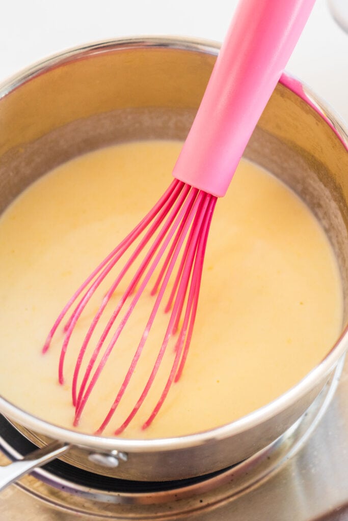 cream sauce being mixed with pink whisk in small saucepan.