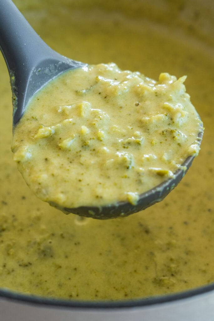 spoon serving cream of broccoli soup out of pot.