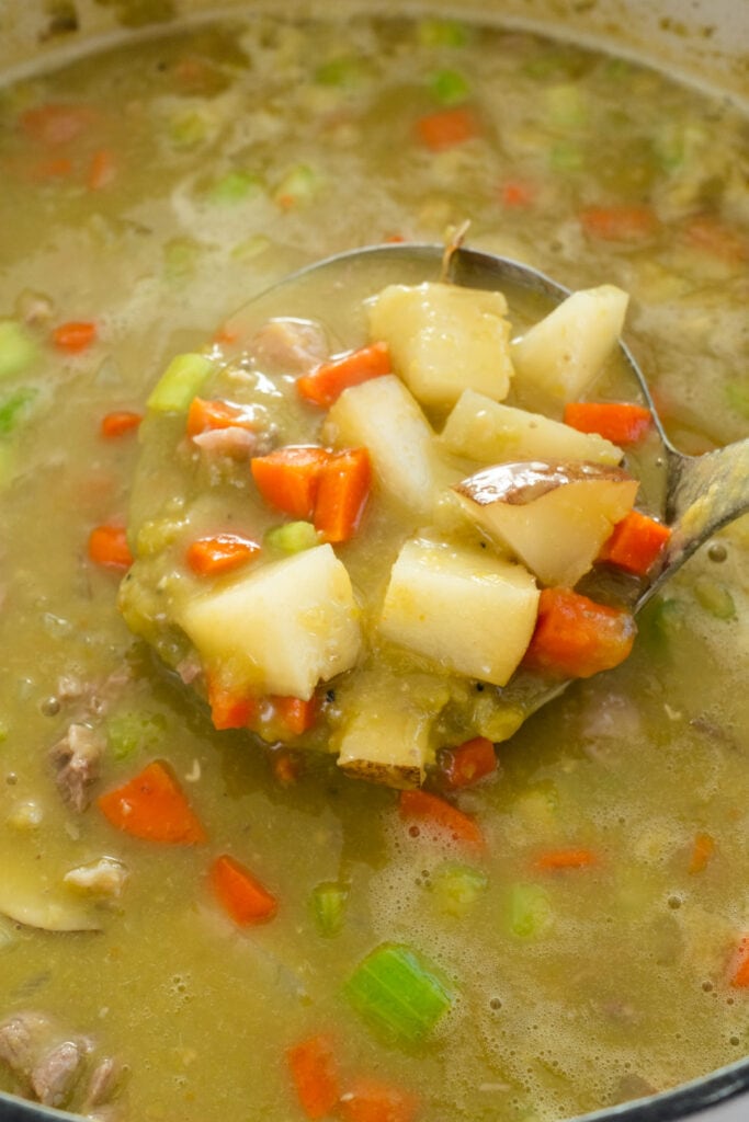 cooked vegetables being spooned out of split pea soup in pot. 