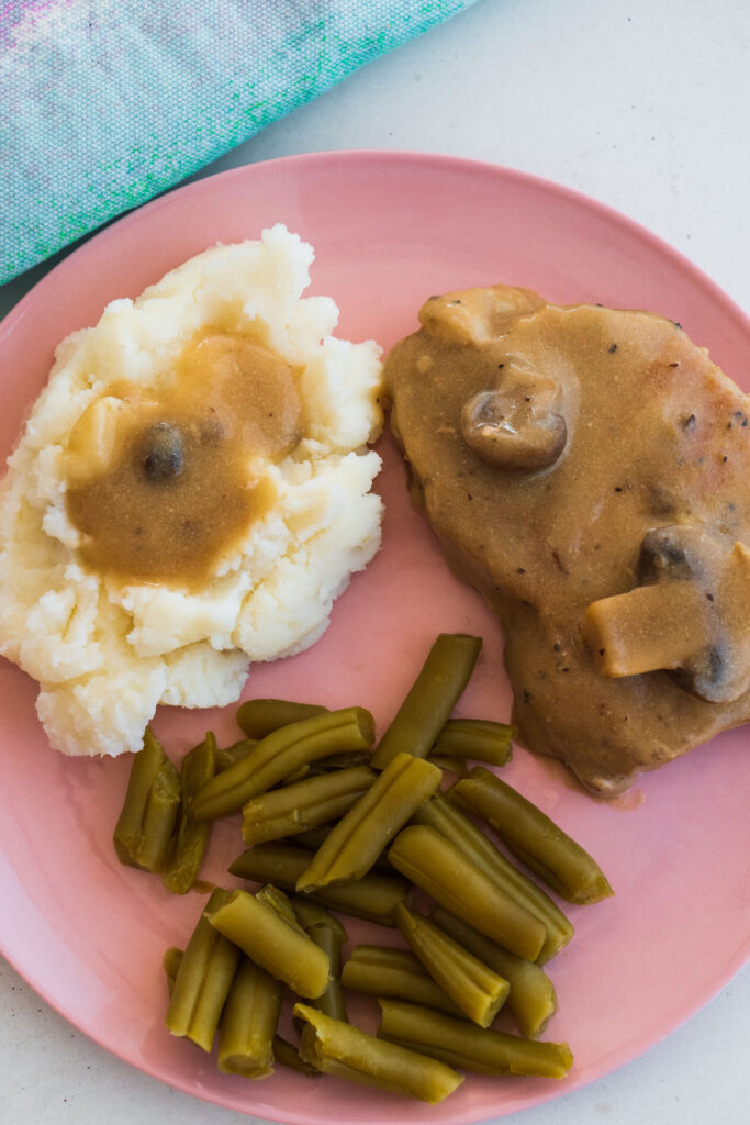 pork chops, mashed potatoes and green beans on pink plate.