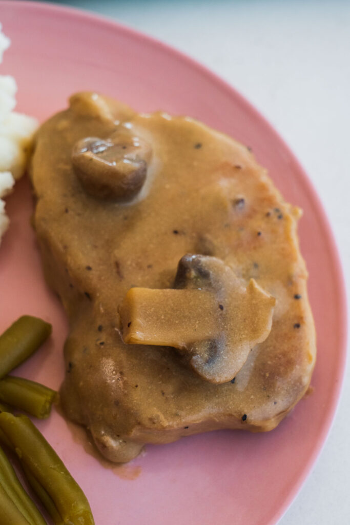 pork chops with gravy and mushrooms on pink plate.