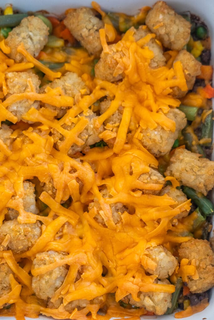 melted cheese on top of casserole  with tater tots and vegetables. 
