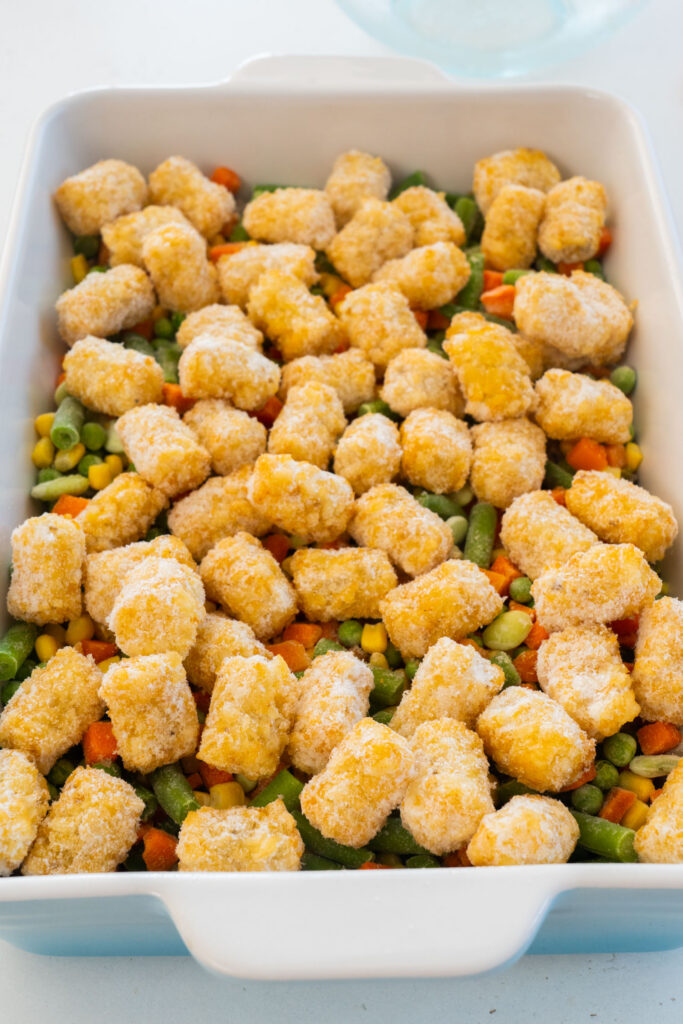 frozen tater tots on top of vegetables in baking dish.